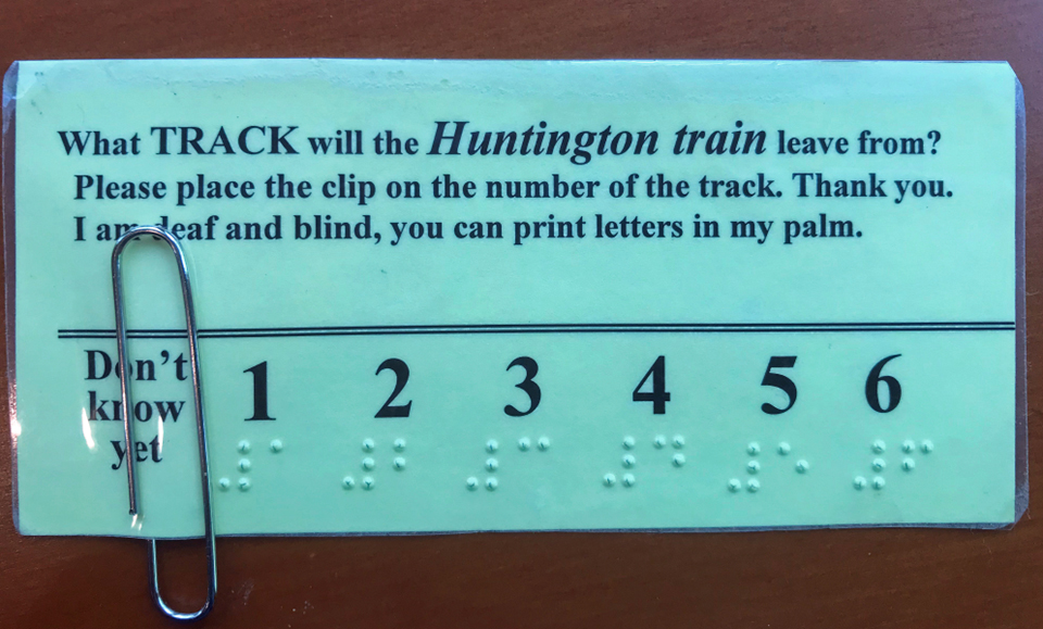 card says,'what track will Huntington Train leave from?  Please place the clip on the number of the track.  Thank you.  I am deaf and blind, you can print letters on my palm.'  Below is a line starting with 'Don't know yet' and then the numbers 1-6 in print and braille, A paper clip is over the 'Don't know yet.'